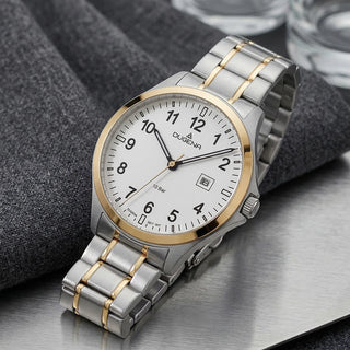  Dugena Boston mit goldfarbener Lünette, Datumsanzeige und Bicolor-Edelstahlband auf einer Metallfläche neben grauem Stoff