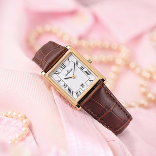 Dugena Quadra Classica 4461119 mit goldfarbenem Gehäuse und braunem Lederband, auf rosa Stoff neben Perlen arrangiert